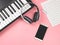 Flat lay of  mobile phone , blank music sheet and  headphones on electric piano on pink background with copy space.Remote piano