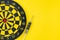 Flat lay of perfect black darts with dartboard on solid yellow background with copy space using as only one business chance to