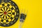 Flat lay of perfect black darts with dartboard on solid yellow background with copy space using as target and goals or three best