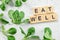 Flat lay photo - leaves of cornsalad Valerianella locusta with text EAT WELL at wooden blocks on white working board. Green