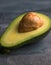 Flat lay photoshot of halved green avocado with a stone on the grey background