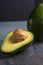 Flat lay photoshot of halved green avocado with a stone on the grey background