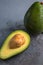 Flat lay photoshot of halved green avocado with a stone on the grey background