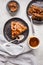 Flat lay of pieces of homemade snickers cake with chocolate cream and caramel on a black saucer, white background