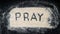 Flat lay of PRAY text written on white sand