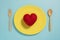 Flat lay of red heart on yellow plate with fork on pastel blue color background