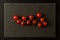 Flat lay. Sprig of cherry tomatoes on a black cutting board. Black background