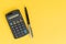 Flat lay or top view of black pen with calculator on vivid yellow background table with blank copy space, math, cost, tax or