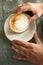 Flat lay, top view of men`s hands holding a cappuccino milk foam glass standing on a metal table surface. Working energy boost