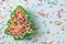 Flat lay view of Christmas tree shaped cookie cutter filled with rainbow sugar sprinkles.