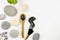 Flat lay view of mud charcoal mask on wooden spoon and smear on white background, surrounded with beauty brush and flat sea stones