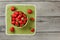 Flat lay view - small bowl with strawberries, some spilled on green tablecloth, gray wood desk under