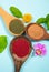 Flat lay view of various superfood powders on spoon decorated with flower blossoms and leaves on blue studio background.