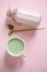 Flat lay. White ceramic cup of whipped matcha latte, bamboo scoop with powdered green tea, bottle of healthy vegan milk