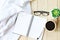 Flat lay of white knitted blanket, cup of coffee and blank notebook paper on wooden background