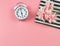 Flat lay of white vintagae alarm clock  with bouquet of pink flower on black and white stripes cloth on pink background with copy