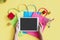 Flat lay of woman hands using tablet with miniature gift boxes. trolley and colorful bags on yellow background. Top view and copy