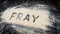 Flat lay of word PRAY written on white sand