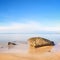 Flat rock on golden beach and sea. Long exposure.