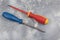Flat screwdriver with insulator, magnetic and with red and yellow handle and phillips with blue handle on cement surface