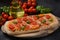 Flatbread pizza garnished with fresh cherry tomatoes, basil, cheese and olive oil on wooden pizza board.