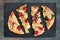 Flatbread pizza with mozzarella, tomatoes, spinach and artichokes on slate