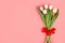 Flatlay beautiful bouquet of white tulips tied with a red ribbon isolated on a pastel pink background with copyspace