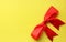 Flatlay beautiful red bright four-contour festive gift bow of satin ribbon on a yellow background. Holiday and packaging. View