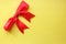 Flatlay beautiful red bright four-contour festive gift bow of satin ribbon on a yellow background. Holiday and packaging. View