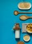 Flatlay with a bottle of rice milk, corn flakes and dried fruit on a bright blue background with space, vertical