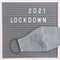 Flatlay letter board with message text lockdown 2021 and grey cloth protective face mask. Lock down loading concept