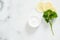 Flatlay organic dermatology cosmetic hygienic cream in glass jar, parsley, citrus lemon on white marble background. Skincare