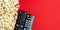 Flatlay of  popcorn and  TV remote control on a red background.