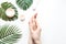 Flatlay. Woman putting nutritious cream on her hands on white background among jar of cosmetic cream, leaf palm branch