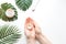 Flatlay. Woman putting nutritious cream on her hands on white background among jar of cosmetic cream, leaf palm branch