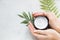 Flatlay. Woman putting nutritious cream on her hands on white background among jar of cosmetic cream, leaf palm branch