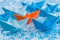 Fleet of blue Origami paper ships on blue water like background surrounding an orange one