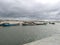 A fleet of fishing boats are moored together alongside a wharf and there are buildings above. Boat filled with sand