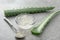 Flesh of aloe in bowl with fresh leaves on grey table