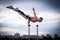 Flexible acrobat doing handstand on the cityscape background with dramatic clouds. Concept of willpower, control and