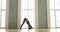 Flexible girl practicing yoga performs asanas in light class near large window.