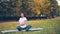 Flexible girl yogini is practising simple twist pose then resting in lotus position sitting on yoga mat on grass in park