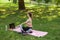 Flexible lady does body twist sitting near open laptop on pink mat in summer park