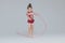 Flexible little girl in beautiful red dress is doing gymnastic exercises with ribbon on grey background