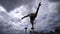 Flexible male circus Artist turning and keep balance by one hand on the rooftop against amazing cloudscape. Movement