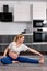 flexible pregnant lady in sportive outfit stretching legs while sitting on floor in kitchen