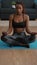 Flexible slim black woman sitting in lotus position on yoga map in living room