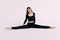 Flexible slim woman gymnast in black sportswear doing splits  on white background