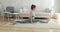 Flexible sporty young woman making longitudinal split sitting in carpet at home.