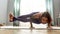 Flexible woman in tight sportswear looking focused, practicing yoga, doing Eight Angle pose while exercising in living